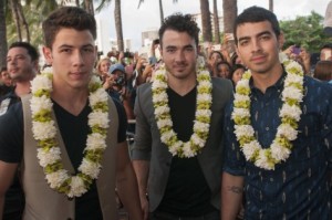 Nick, Kevin e Joe dos Jonas Brothers posam para uma foto na chegada à estreia da quarta temporada de Hawaii Five-0, na Queen's Beach, em Waikiki, Havai - 26 de setembro de 2013. GETTY IMAGES/CBS/Norman Shapiro.