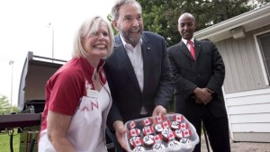 O líder Federal do NDP Tom Mulcair, ao centro, mostra queques caseiros Canadá no James Jardins Lawn Bowling Club em Toronto - 1 de julho de 2015. (Darren Calabrese / The Canadian Press)