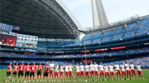 Membros da equipa de basebol feminino do Canadá, a competir nos Jogos Pan-americanos, acenam para a multidão antes do início do jogo de basebol MLB entre os Toronto Blue Jays e os Tampa Bay Rays, no sábado 18 de julho, 2015 em Toronto. THE CANADIAN PRESS/Jon Blacker