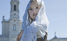 Uma criança vestida de pastorinha de Fátima segura ao colo uma figura de uma ovelha