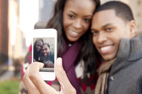 Foto de arquivo de um jovem casal a tirar uma foto num telemóvel. Cavan Images.