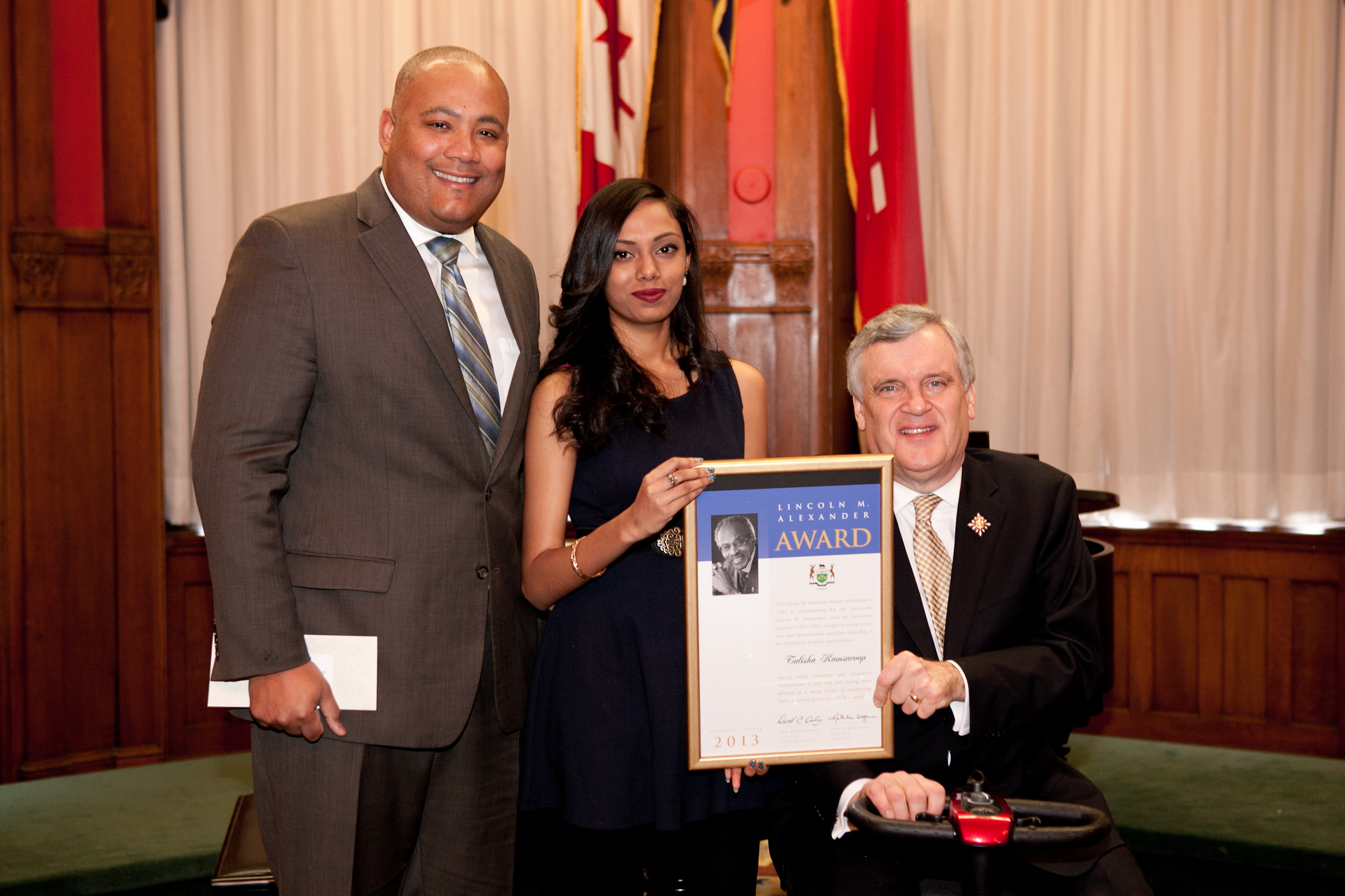 Talisha Ramsaroop recebe o Lincoln M. Alexander Community Award, de Michael Coteau, o ministro da Cidadania e Imigração, e David C. Onley, vice-governador do Ontário