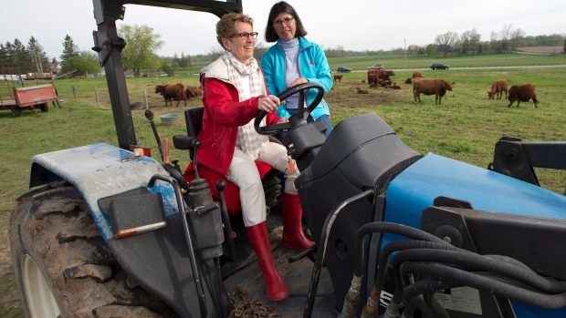 Kathleen Wynne conduz um tractor com instrução da agricultora Sandra Vos (à direita), num evento de campanha em Paris, Ontário, na terça-feira 20 de maio de 2014. THE CANADIAN PRESS/Frank Gunn
