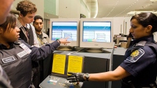 A oficial da CBSA, Nav Rogers, à direita, e a Acting Chief of Enforcement, Joycelyn Jeffers, segunda à esquerda, examinam uma imagem X-Ray de um pedaço suspeito de bagagem, durante uma demonstração por parte da Agência de Serviços de Fronteiras do Canadá, no aeroporto Pearson, em Toronto - 9 de agosto de 2011. The Canadian Press / Aaron Vincent Elkaim