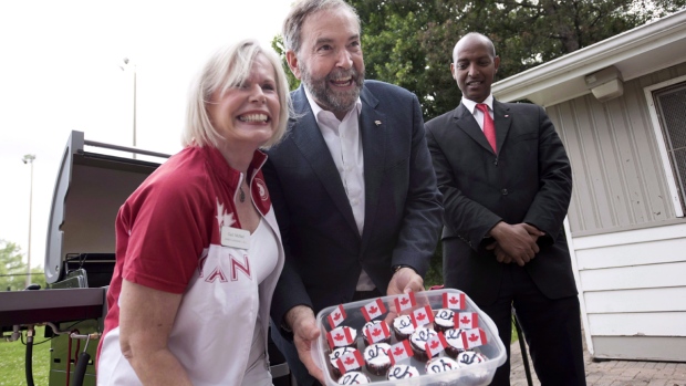O líder Federal do NDP Tom Mulcair, ao centro, mostra queques caseiros Canadá no James Jardins Lawn Bowling Club em Toronto - 1 de julho de 2015. (Darren Calabrese / The Canadian Press)