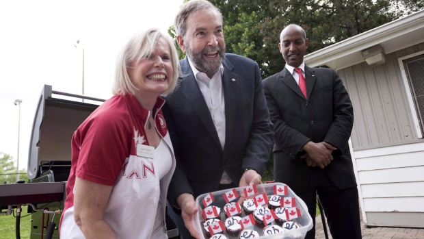 O líder Federal do NDP Tom Mulcair, ao centro, mostra queques caseiros Canadá no James Jardins Lawn Bowling Club em Toronto - 1 de julho de 2015. (Darren Calabrese / The Canadian Press)