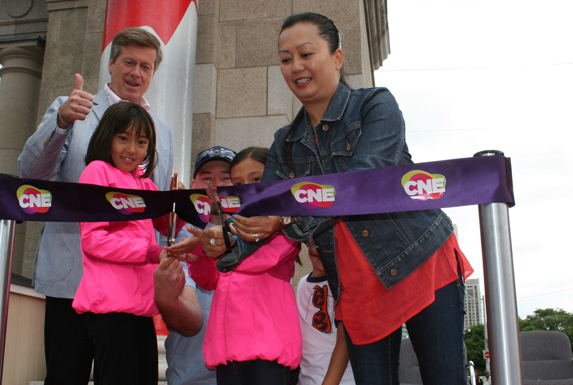 O corte da fita durante a cerimónia de abertura oficial da Canadian National Exhibition no dia 21 de agosto de 2015 com o presidente de Toronto John Tory e a primeira família cerimonial. Mãe e pai são Patrick e Maria Eichenberg, junto com as crianças (da esquerda para a direita) Sydney, 9, Alana, 7, e Samuel, 4. LA/CMC