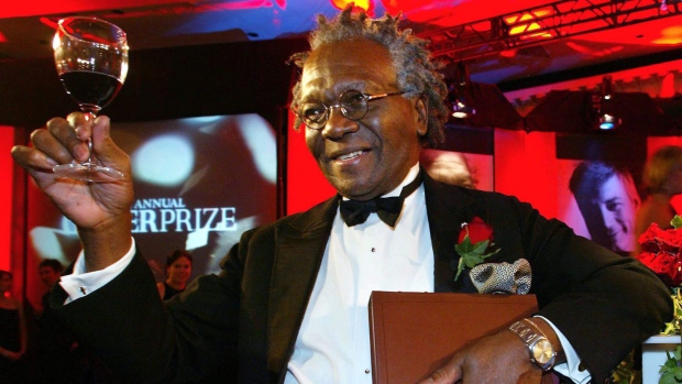 O vencedor do Prémio Giller, Austin Clarke, ergue uma taça de vinho, enquanto segura uma cópia do seu livro - Polished Hoe - depois de vencer o prémio literário no Hotel Four Seasons, em Toronto - 5 de novembro de 2002. (Kevin Frayer / The Canadian Press)