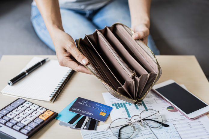 Stressed young woman open her empty wallet and calculating expenses at home