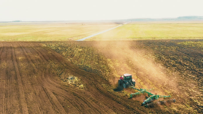 4K Aerial Elevated View.Tractor Plowing Field. Beginning Of Agricultural Spring Season. Cultivator Pulled By A Tractor In Countryside Rural Field Landscape