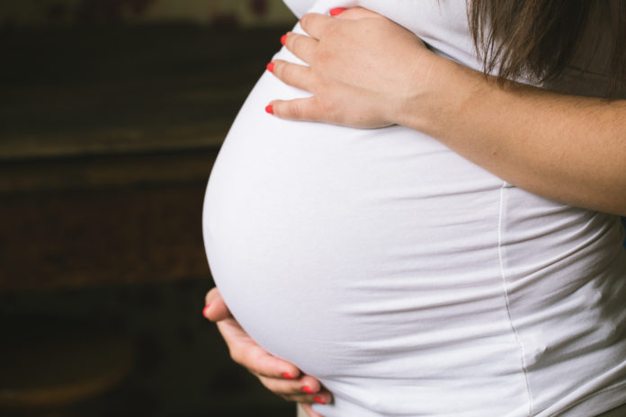 Young pregnant woman holds her hands.