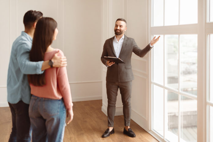 Estate Agent In Suit Showing Buyers New Empty Apartment