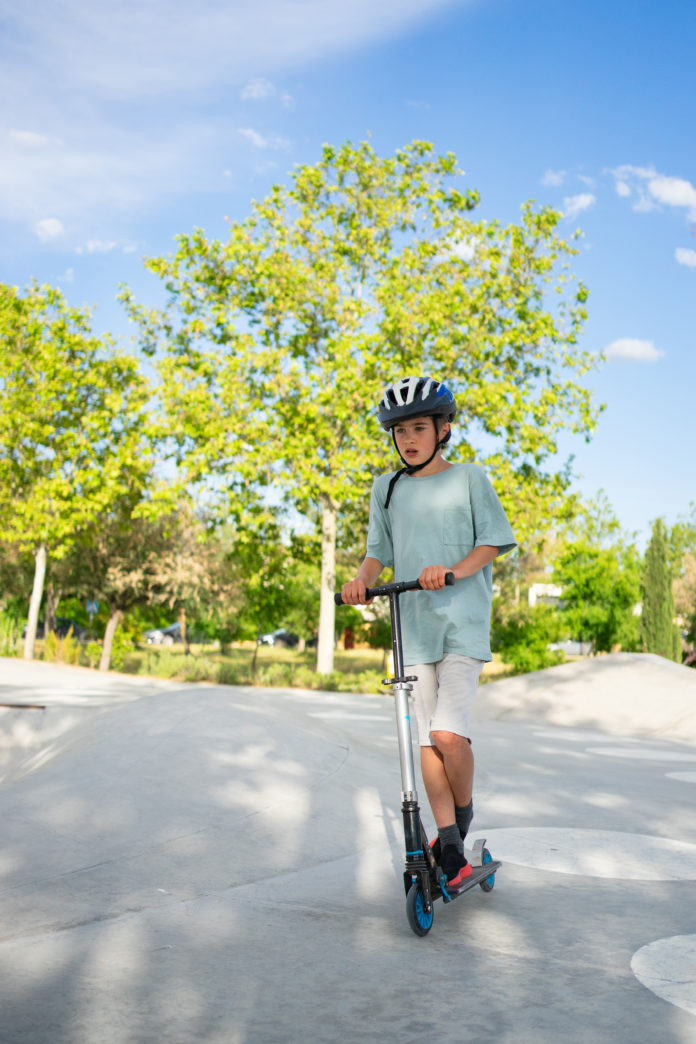 Boy wearing helmet riding scooter in skate park on sunny day