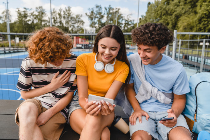 Group of friends laughing out watching video using smart phones handing out in sport court