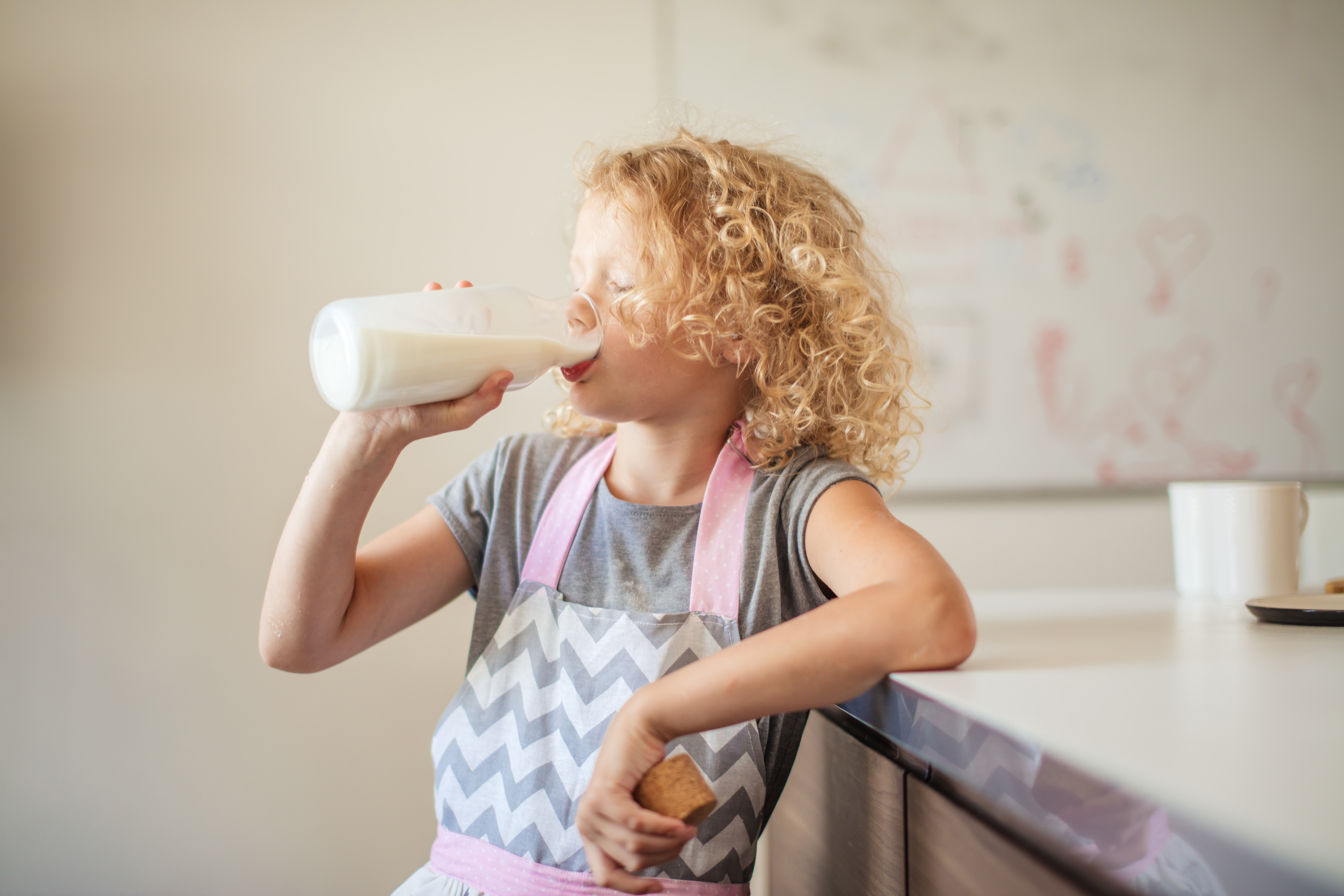 Cute little girl with glass of milk on color background