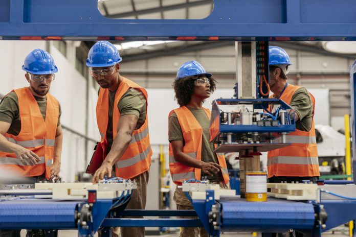Multiracial engineers working on robotic arm in factory