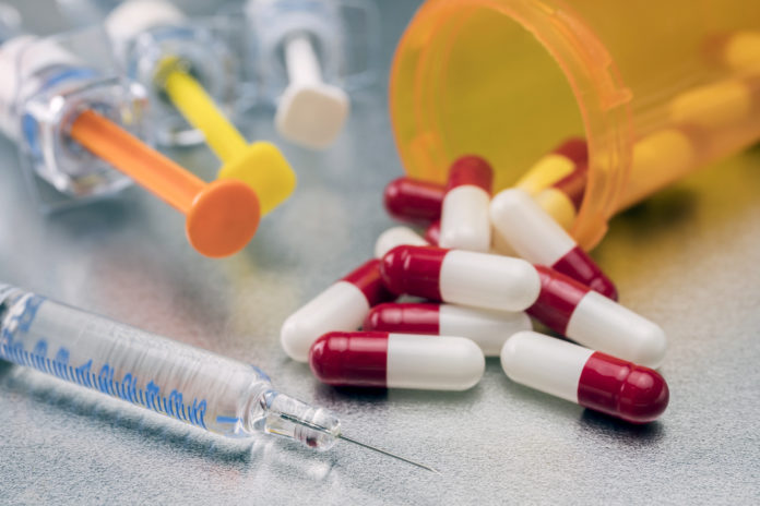 Syringes of several types along with boat of white and red pills, conceptual image