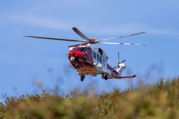 Rescue helicopter flying over grassy area with clear blue sky.
