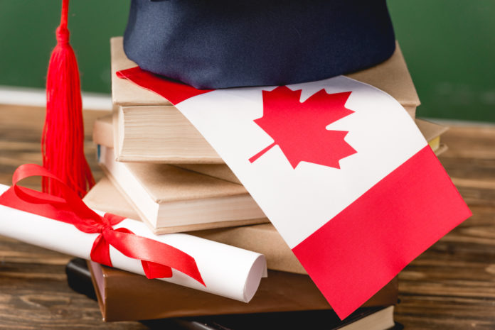 academic cap, books, diploma and canadian flag wooden surface on green