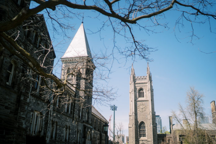 University of Toronto Gothic towers with bare tree branches Gothic-style university buildings with towers and bare trees against a blue sky.